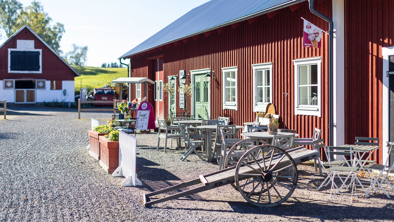 Uteservering vid röd gårdsbyggnad med bord, stolar och kullerstensgård.